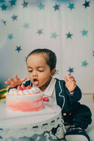 Dressed in black and white jacket boy with pink cake in his hand
